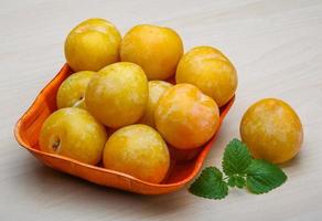 Yellow plums in a bowl on wooden background photo