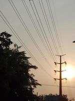 el sol al atardecer con siluetas de postes eléctricos y farolas. foto