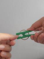 A hand tries to pinch his thumb using a green clothespin. photo