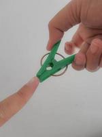 A hand tries to pinch his thumb using a green clothespin. photo