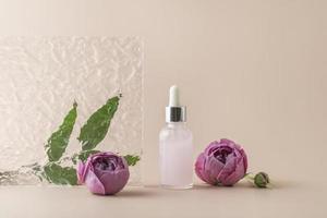 A face serum or essential oil in a pink dropper bottle standing on a beige background with rose petals around it photo