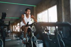 Asian sportsman exercising on a bicycle in the gym, determination to cardio lose weight, makes her healthy. exercise bike man fitness sport concept. photo