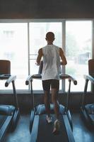 Back side of asian athlete sportsman runner tan skin running on treadmill in fitness club. Cardio workout. Healthy lifestyle, guy training in gym. Sport running concept. photo