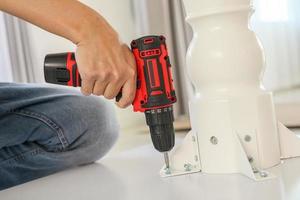 man assembling white table furniture at home using cordless screwdriver photo