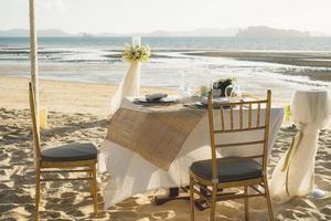 hermosa mesa preparada para una cena romántica en la playa con flores y velas. catering para una cita romántica, una boda o un fondo de luna de miel. cena en la playa al atardecer. foco seleccionado. foto