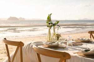 Beautiful table set up for a romantic dinner on the beach with  flowers and candles. Catering for a romantic date, wedding or honeymoon background. Sunset beach dinner. selected focus. photo