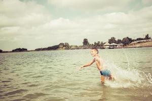 niño despreocupado corriendo en el agua durante el día de verano. foto