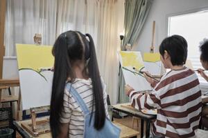 Group of multiracial little children concentrates on acrylic color picture painting on canvas in an art classroom and creatively learns with talents and skill at elementary school studio education. photo