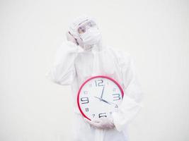 retrato de médico o científico con uniforme de suite ppe sosteniendo un despertador rojo y mirando a la izquierda en varios gestos. covid-19 concepto aislado fondo blanco foto