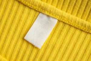 White blank clothing tag label on new yellow shirt background photo