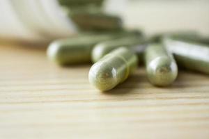 Herbal medicine capsules with bottle on wood table photo