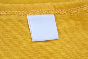 White blank clothing tag label on new yellow shirt background photo
