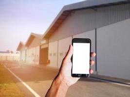 worker hand holding black smartphone with blank screen behind of Industrial factory building with blur background. Space for text or design photo