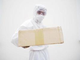 Young man in PPE suite uniform while holding cardboard boxes in medical rubber gloves and mask. coronavirus or COVID-19 concept isolated white background photo