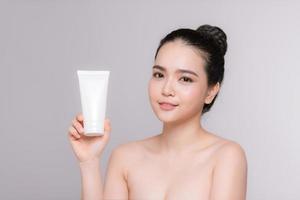 Beautiful asian young woman face portrait holding and presenting cream tube product photo