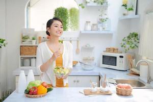 Portrait of smiling young lady cooking fresh organic salad at home in modern kitchen, using and looking at tablet photo