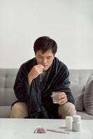 Handsome young man with pill and glass of water at home photo