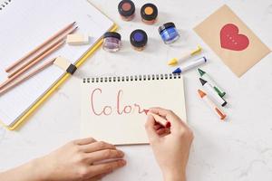 Hand with color pencils and blank sheet of paper on white table photo