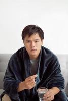 Handsome young man with pill and glass of water at home photo