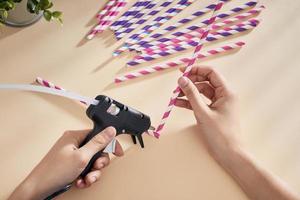 Glue gun in the woman's hand. Woman glues straws with a glue gun. closeup photo