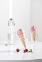 Waffle cone filled with fresh raspberry ice cream in glass cup with fresh raspberry sitting on tabletop photo