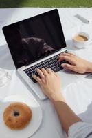 Hands man on laptop keyboard and coffee with donut. Easy work life style at home in the morning. photo