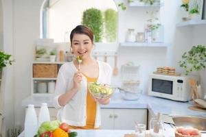young smiling woman eating vegetables salad at kitchen photo