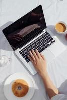 Hands man on laptop keyboard and coffee with donut. Easy work life style at home in the morning. photo