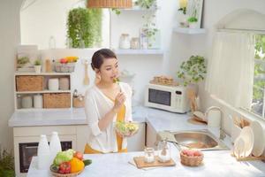 hermosa mujer sonriente comiendo ensalada vegetariana orgánica fresca en la cocina moderna foto