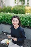 A young cute girl sitting in the park working scrolling a tablet photo