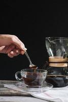 Drip brewing coffee concept. Wooden desk with chocolate cake and cup of coffee on black background. photo