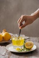 Ginger tea with lemon, ginger root and rosemarry on wooden background. Small glass transparent pitcher with hot drink. Seasonal beverages. Shallow DOF, selective focus, focus on top of pitcher. photo