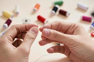 people, needlework, sewing and tailoring concept - tailor woman with thread in needle stitching fabric. Hands sewing with a needle and thread. Fingers pulling thread into the needle photo