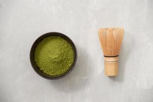 Matcha, green tea powder in black bowl with bamboo whisk on slate background. Top view. photo