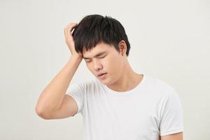 A young man holding his head with his hand looks tired with a headache, isolated on a white background. photo
