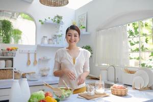 Beautiful young woman making tasty salad in kitchen, photo
