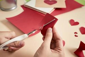 woman cuts out red felt hearts, homemade crafts for Valentine's day, hand made creativity, top view photo