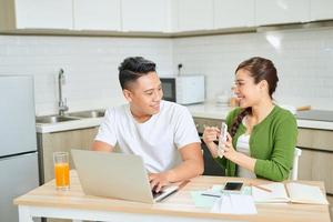 Young couple managing finances, reviewing their bank accounts using laptop computer and calculator at modern kitchen. photo