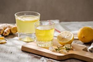 Refreshing summer drink with lemon, ginger, rosemary and ice on rustic wooden table, copy space photo