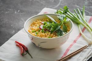 Instant noodles in bowl with radish, herbs and onion photo