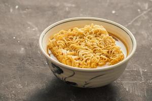 Instant noodles in bowl and vegetable side dishes on stone background. Quick and easy food concept. photo