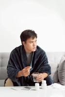 Handsome young man with pill and glass of water at home photo