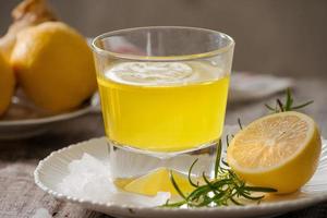 Ginger tea with lemon, ginger root and rosemarry on wooden background. Small glass transparent pitcher with hot drink. Seasonal beverages. Shallow DOF, selective focus, focus on top of pitcher. photo