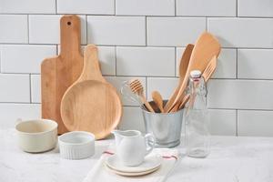 Simple rustic kitchenware against white wooden wall rough ceramic pot with wooden cooking utensil set, stacks of ceramic bowls, jug and wooden trays. photo