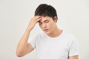 A young man holding his head with his hand looks tired with a headache, isolated on a white background. photo