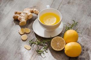 Cup of Ginger tea with lemon. Cup of Ginger tea with lemon. Glass mug of green hot tea on wooden table. Sliced lemons on a chopping board photo