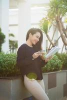 Happy young woman holding book fond of literature analyzing novel during leisure time on terrace of campus cafe in sunny day. photo