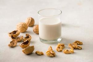 Organic walnut nuts and glass of walnut milk on stone background. photo