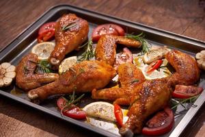 Baked chicken drumstick and wings on baking tray over dark wooden background.