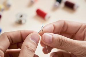 people, needlework, sewing and tailoring concept - tailor woman with thread in needle stitching fabric. Hands sewing with a needle and thread. Fingers pulling thread into the needle photo